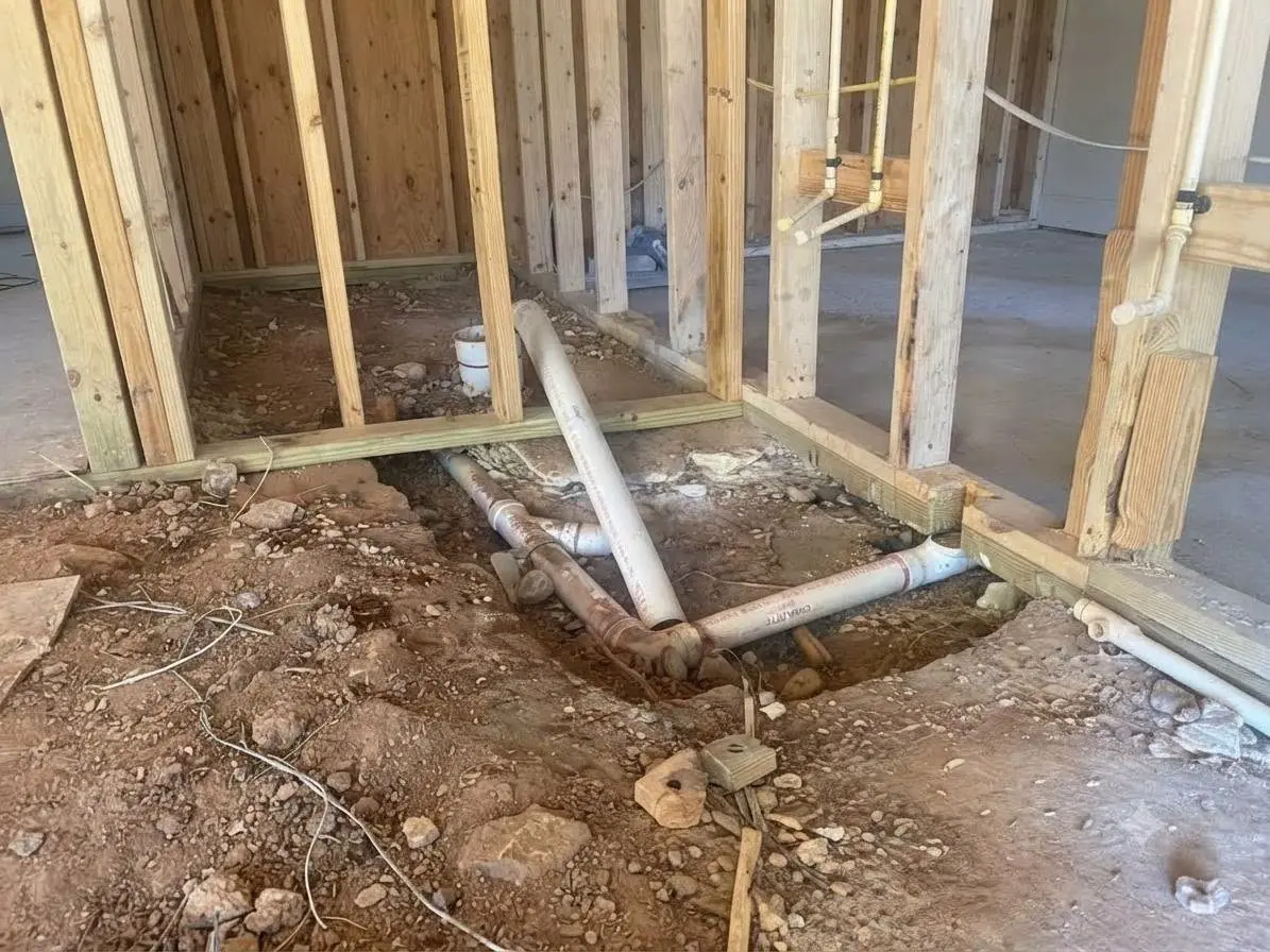 Basement concrete floor opened up to expose drain pipes, with new white plastic drain lines beside the old cast iron
