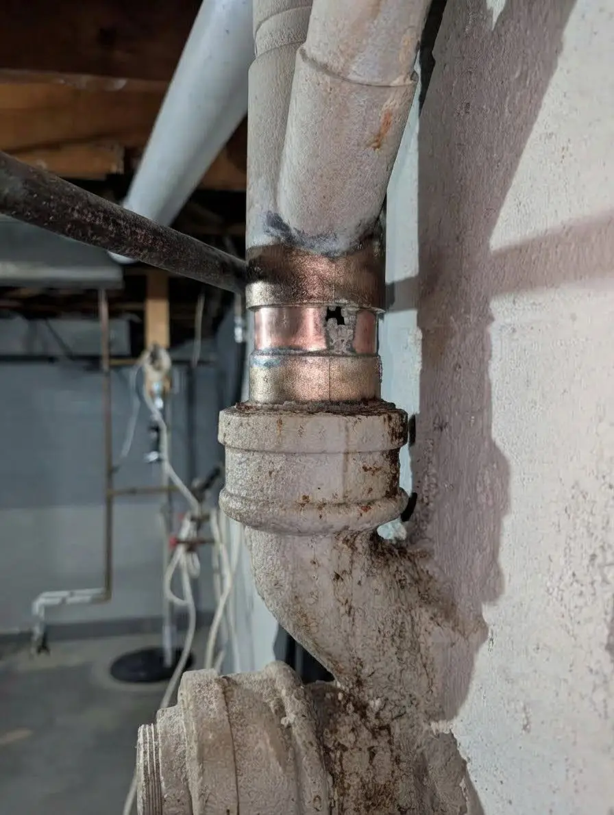 Section of drain pipe in an unfinished basement showing rust staining below a joint and a copper repair